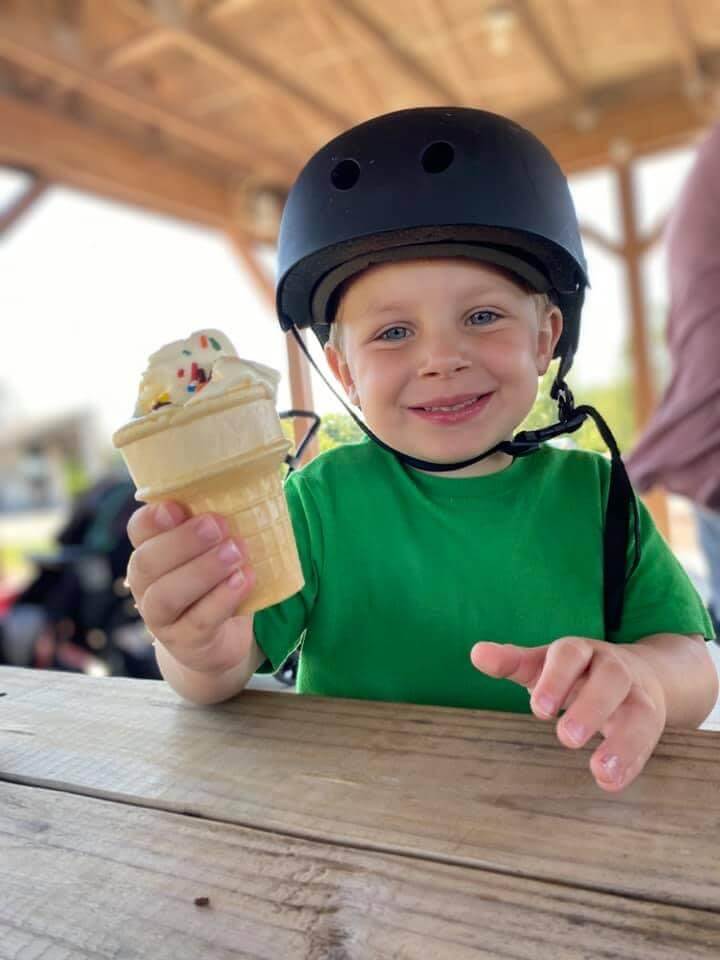 Preschool aged boy wearing a black helmet holding an ice cream cone