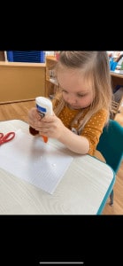 Preschool girl placing glue on a piece of paper