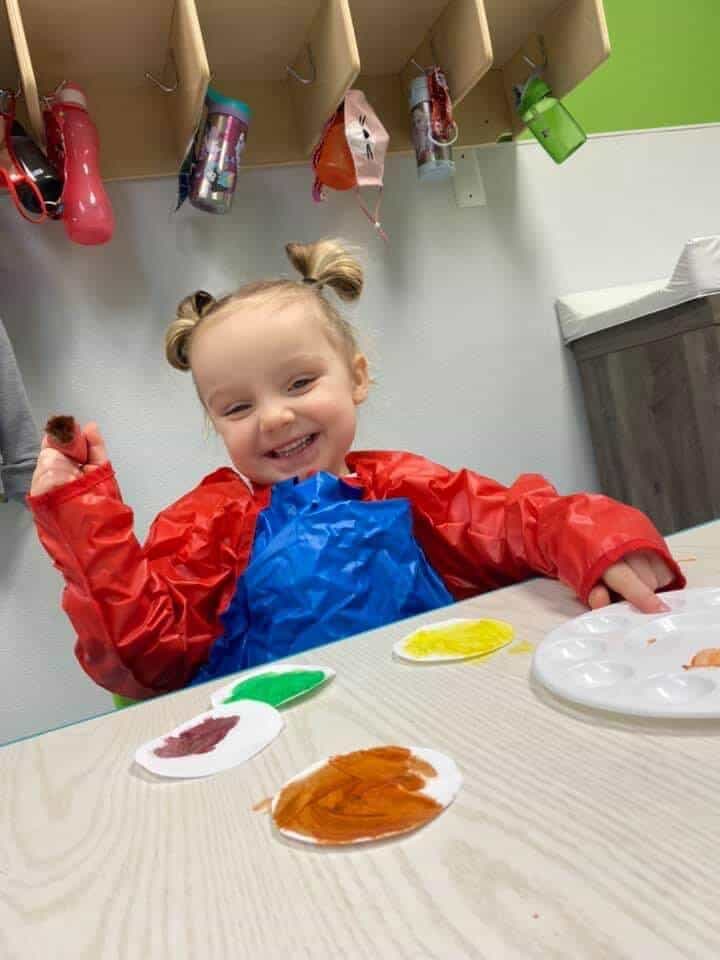 3 year old girl at daycare wearing a red jacket painting