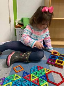 Young girl sitting on the floor playing with magnetic blocks