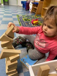 Young girl sitting on the ground playing with wooden blocks